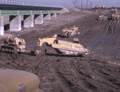 construction machinary digging up soil in front of a bridge